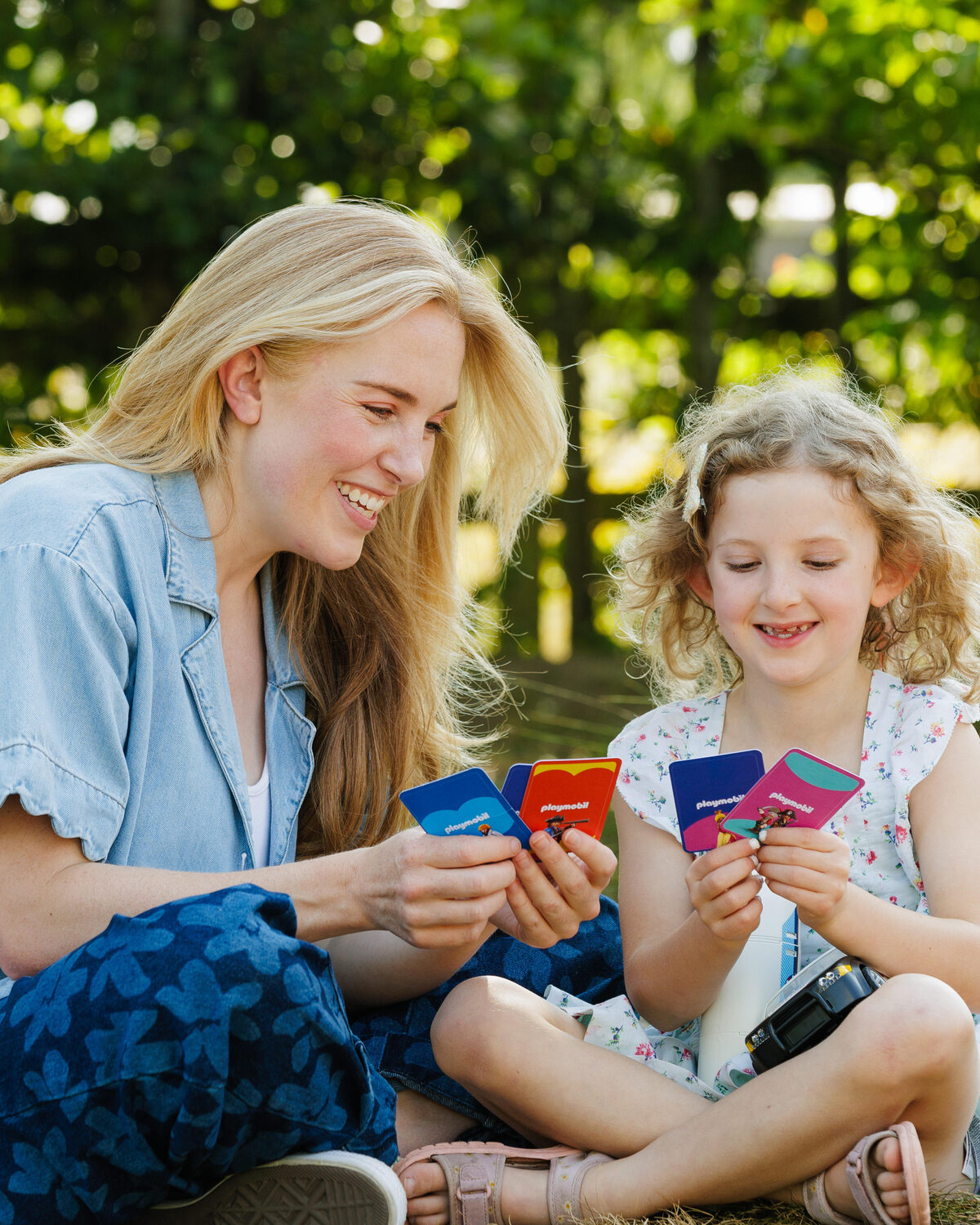 Maddie Moate and a young girl reading Playmobil story prompt cards together outdoors