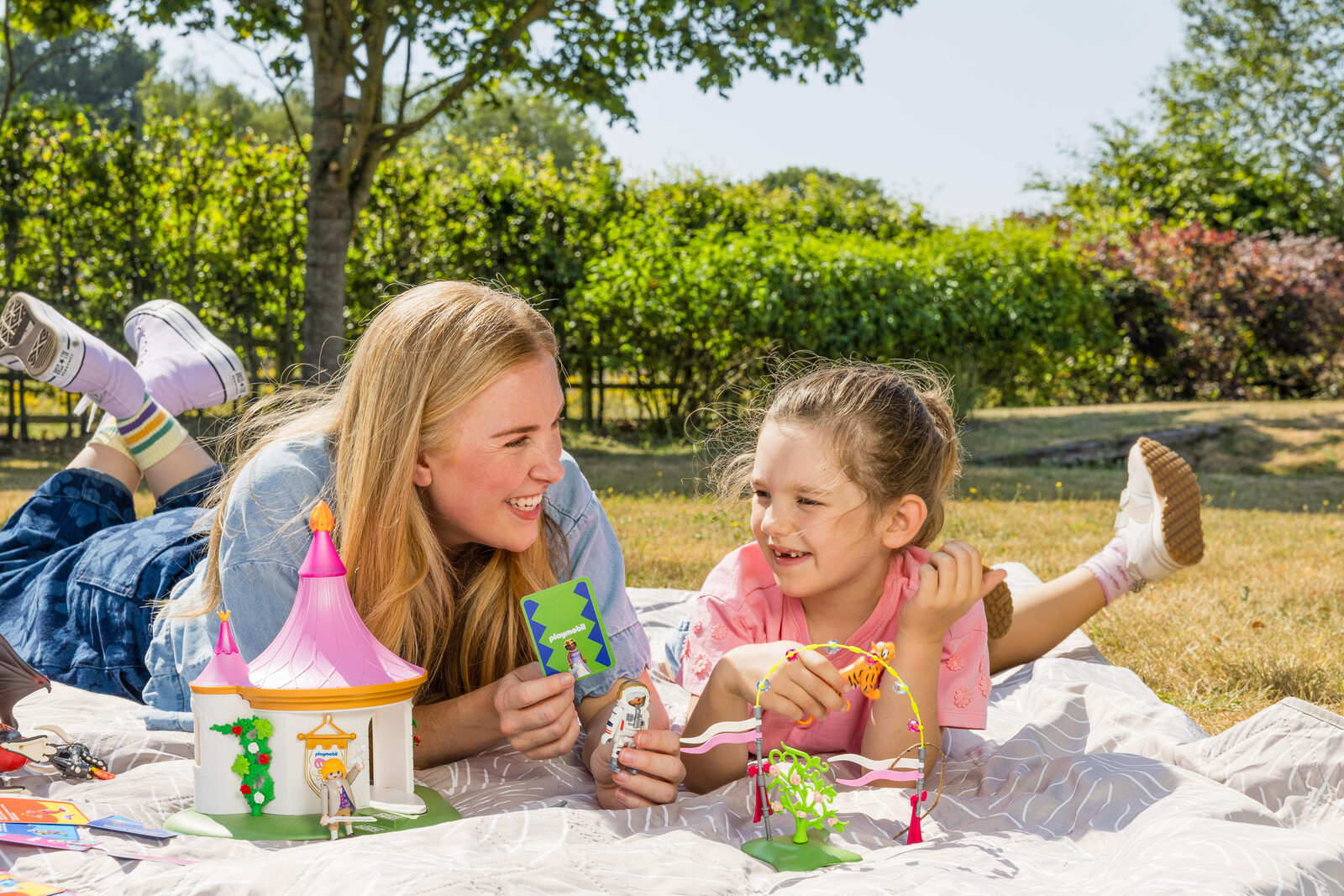 Maddie Moate and a young girl lying on a blanket playing with Playmobil sets and prompt cards